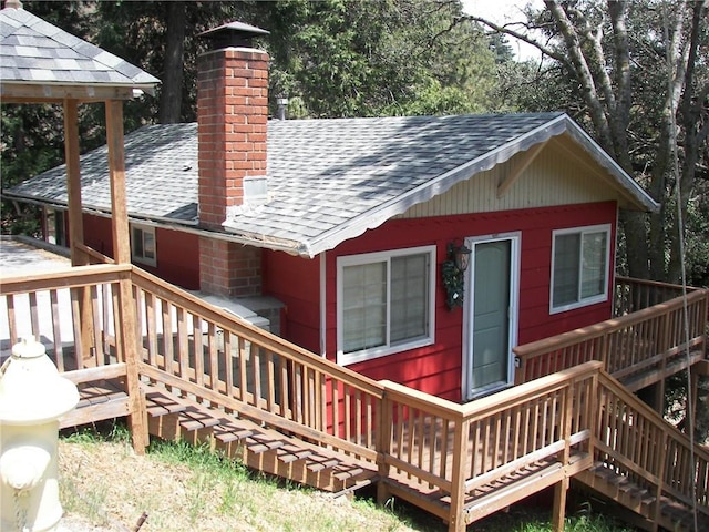 rear view of property with a deck, a chimney, and roof with shingles