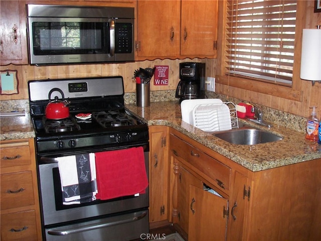 kitchen featuring stainless steel appliances, brown cabinetry, a sink, and water heater