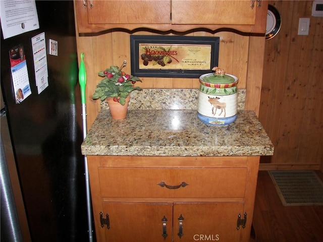 interior details featuring freestanding refrigerator, wood walls, wood finished floors, and visible vents