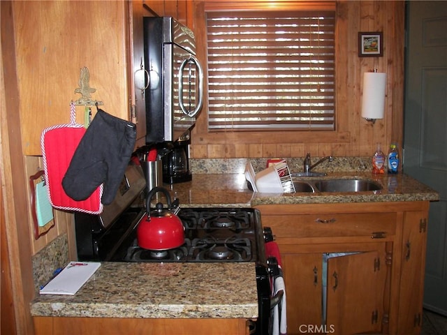 kitchen featuring stainless steel microwave, brown cabinetry, a sink, and range with gas cooktop