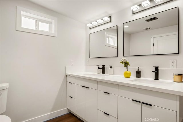 bathroom featuring baseboards, a sink, double vanity, and toilet