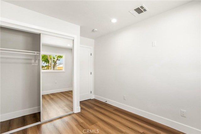 unfurnished bedroom featuring visible vents, wood finished floors, baseboards, a closet, and recessed lighting