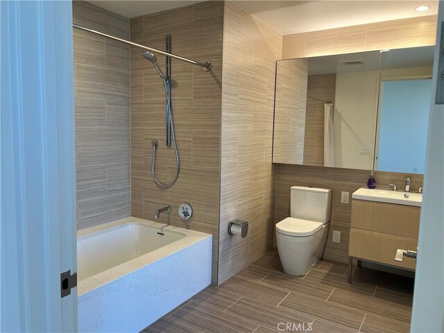 bathroom featuring vanity, shower / bath combination with curtain, toilet, and tile walls