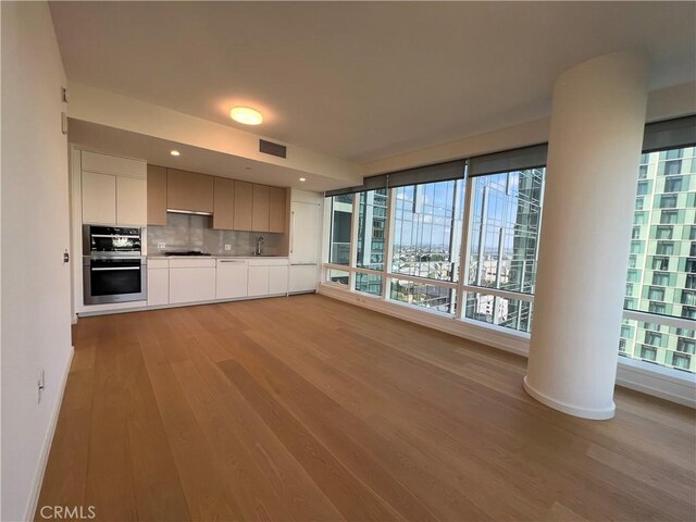 unfurnished living room featuring a sink, light wood-style floors, recessed lighting, baseboards, and visible vents