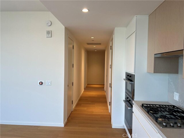 hall with light wood-style floors, recessed lighting, and baseboards