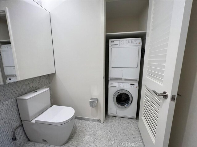 bathroom featuring baseboards, tile patterned floors, stacked washer / dryer, and toilet