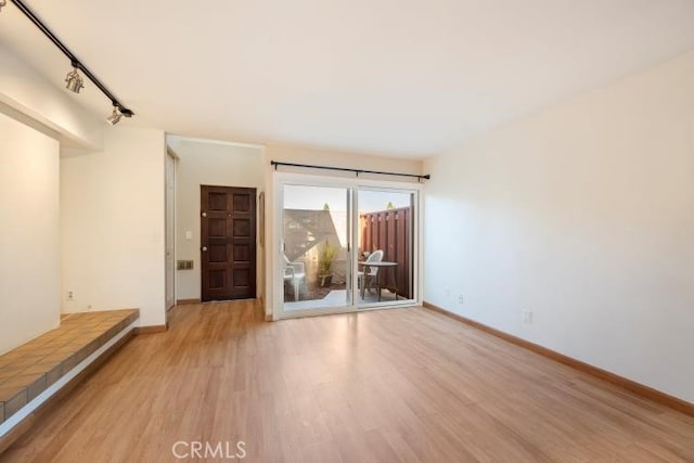 empty room with light wood-style floors, baseboards, and rail lighting