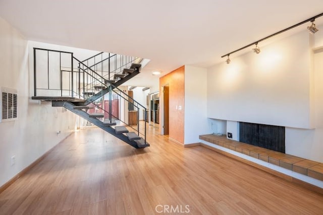 unfurnished living room featuring a fireplace, rail lighting, baseboards, wood finished floors, and visible vents