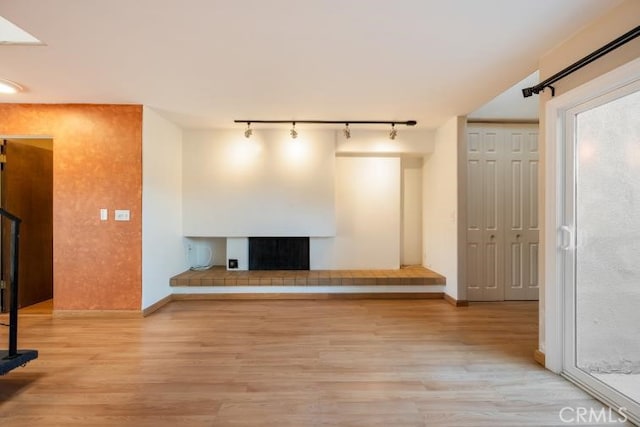 unfurnished living room featuring track lighting, baseboards, a fireplace with raised hearth, and light wood-type flooring