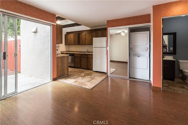 kitchen featuring stacked washer / dryer, stainless steel dishwasher, wood finished floors, a sink, and freestanding refrigerator