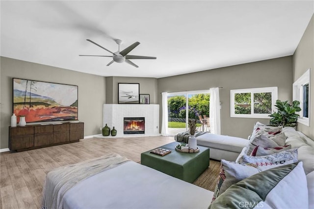 living room featuring baseboards, a brick fireplace, ceiling fan, and wood finished floors