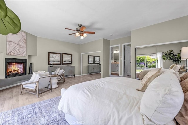 bedroom featuring a warm lit fireplace, ceiling fan, and wood finished floors