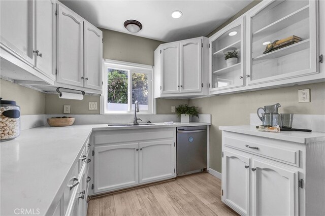 kitchen with light countertops, white cabinets, a sink, light wood finished floors, and dishwasher