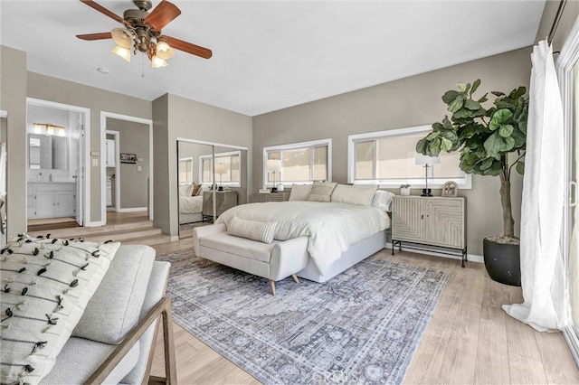 bedroom featuring baseboards, ceiling fan, light wood-type flooring, and ensuite bath