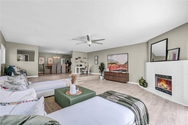 living area with baseboards, wood finished floors, ceiling fan with notable chandelier, and a fireplace