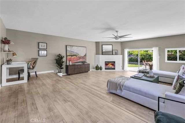 living room with a brick fireplace, a ceiling fan, baseboards, and light wood-type flooring