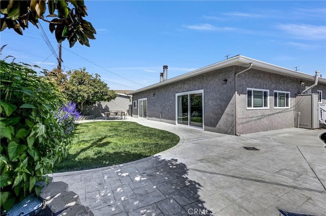 rear view of house with a lawn, a patio area, and stucco siding