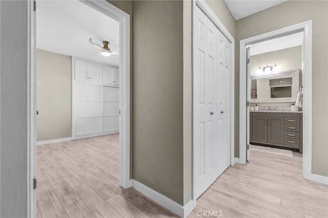 hallway featuring baseboards, a sink, and light wood-style flooring