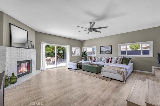 living room featuring a brick fireplace, light wood finished floors, and ceiling fan