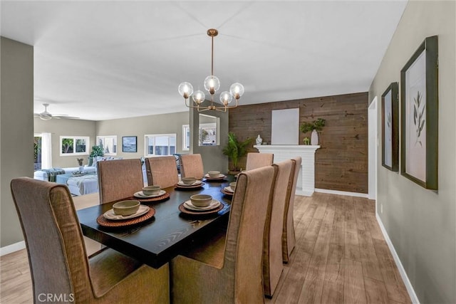 dining area featuring wooden walls, baseboards, ceiling fan with notable chandelier, and light wood-type flooring