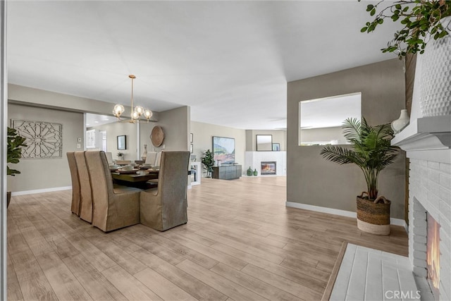 dining area with baseboards, a notable chandelier, light wood finished floors, and a fireplace