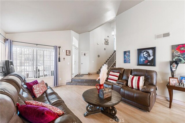 living room featuring high vaulted ceiling, light wood-style flooring, baseboards, visible vents, and stairway
