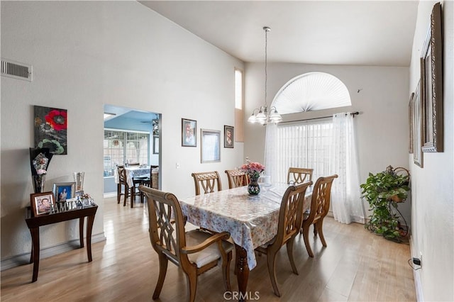 dining space with visible vents, a towering ceiling, baseboards, light wood-type flooring, and ceiling fan with notable chandelier