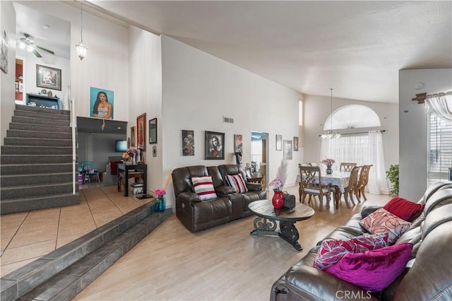 living area featuring visible vents, wood finished floors, stairway, ceiling fan with notable chandelier, and a high ceiling