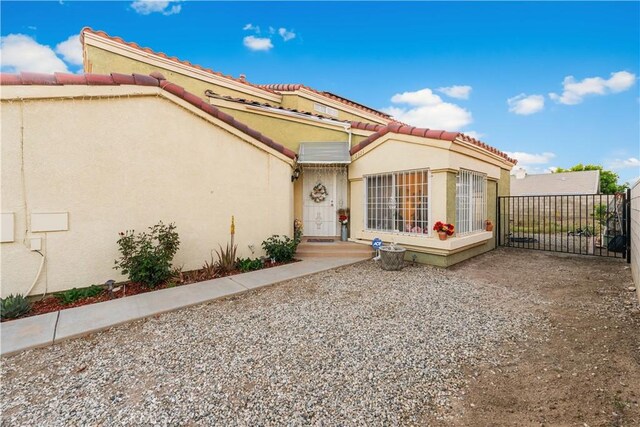 entrance to property with a tile roof, fence, a gate, and stucco siding