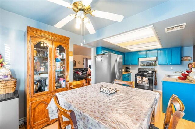 kitchen featuring black range with gas cooktop, freestanding refrigerator, under cabinet range hood, and blue cabinets