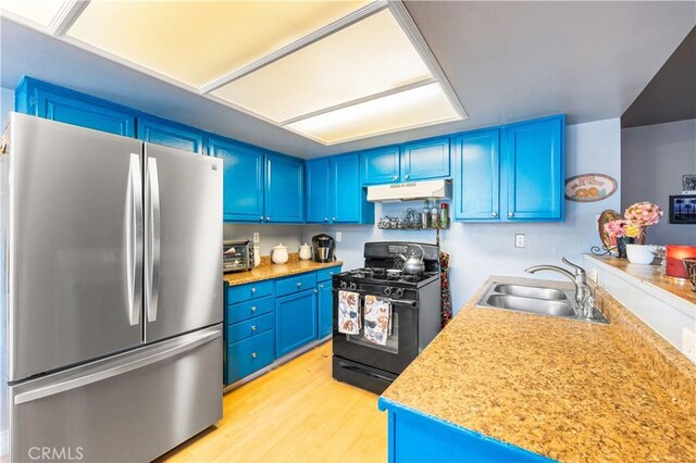 kitchen with a sink, black range with gas stovetop, blue cabinetry, freestanding refrigerator, and under cabinet range hood