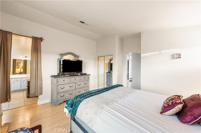 bedroom featuring visible vents, light wood finished floors, ensuite bathroom, and vaulted ceiling