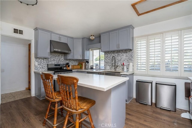kitchen featuring stainless steel range with gas cooktop, gray cabinets, backsplash, and light countertops