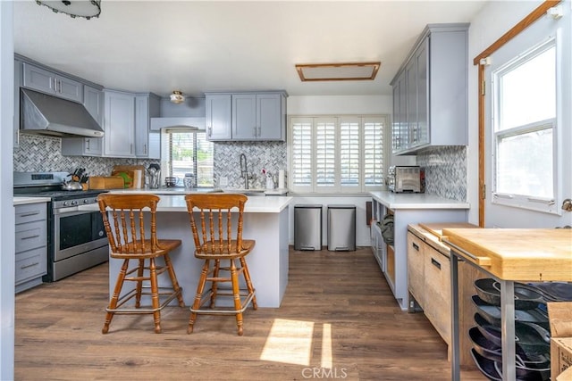 kitchen with stainless steel electric range, under cabinet range hood, gray cabinetry, dark wood-style floors, and light countertops