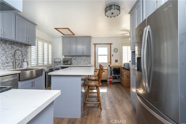 kitchen with appliances with stainless steel finishes, gray cabinetry, a sink, a kitchen bar, and decorative backsplash