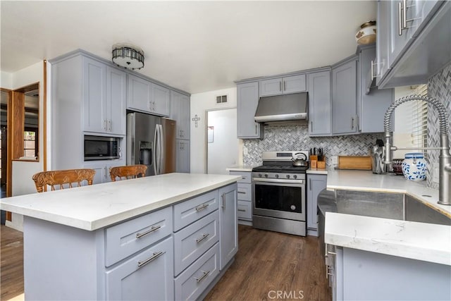 kitchen with appliances with stainless steel finishes, gray cabinetry, under cabinet range hood, and dark wood-style flooring