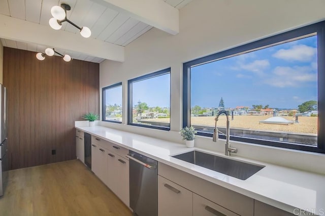 kitchen with beam ceiling, a sink, light countertops, wood walls, and light wood-type flooring