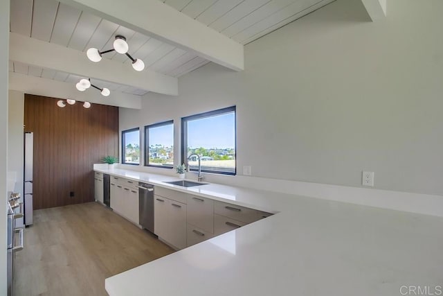 kitchen featuring stainless steel dishwasher, freestanding refrigerator, beam ceiling, a sink, and light wood finished floors
