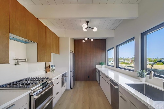 kitchen featuring appliances with stainless steel finishes, a sink, under cabinet range hood, beamed ceiling, and modern cabinets