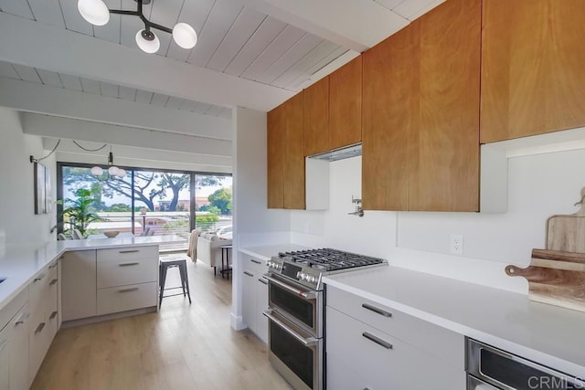 kitchen featuring beamed ceiling, modern cabinets, light countertops, range with two ovens, and light wood finished floors