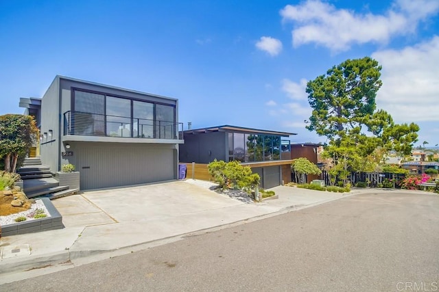 modern home with fence, an attached garage, driveway, and a balcony