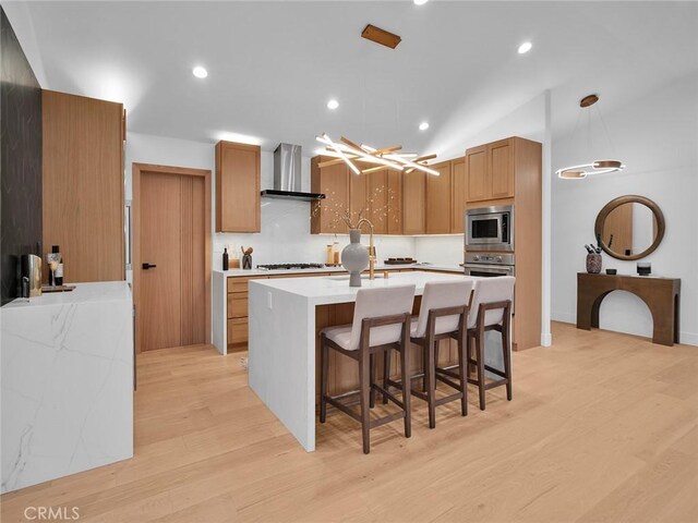 kitchen with wall chimney range hood, light wood-style floors, stainless steel appliances, decorative light fixtures, and decorative backsplash