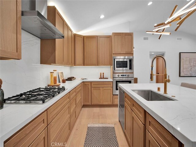 kitchen with backsplash, appliances with stainless steel finishes, vaulted ceiling, a sink, and wall chimney exhaust hood