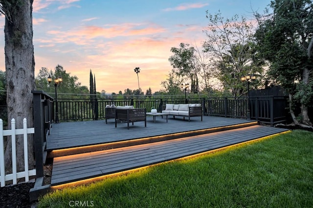 deck at dusk featuring an outdoor hangout area, fence, and a lawn