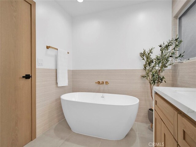 full bathroom with tile walls, tile patterned flooring, wainscoting, vanity, and a soaking tub