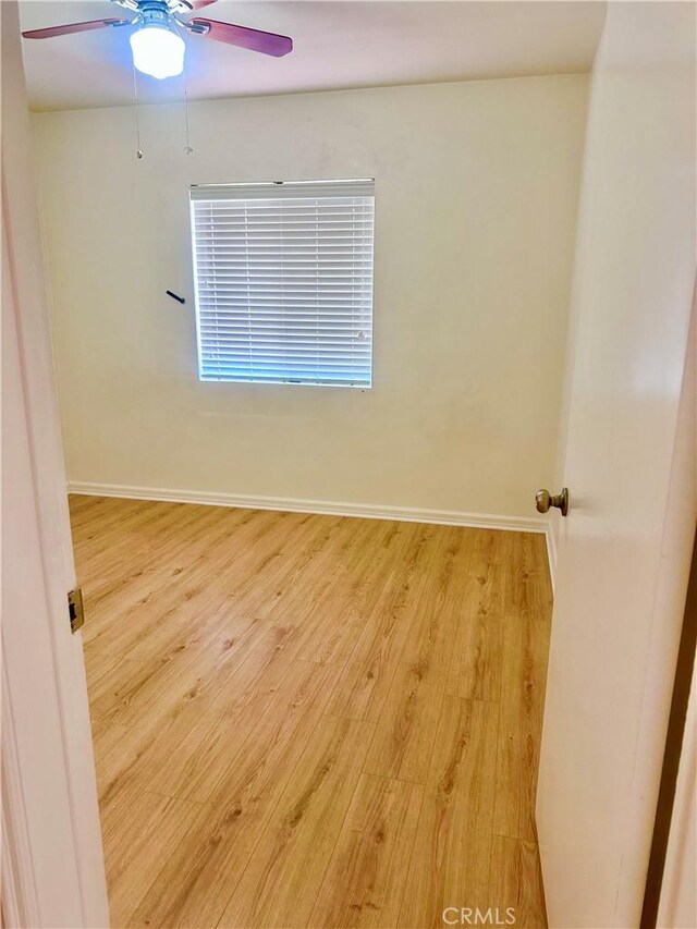 unfurnished room with a ceiling fan, baseboards, and light wood-style flooring
