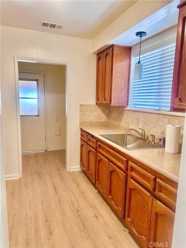 kitchen featuring brown cabinets, visible vents, a sink, and light wood-style flooring