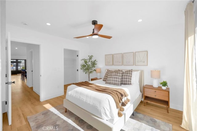 bedroom with light wood-style floors, baseboards, a walk in closet, ceiling fan, and recessed lighting
