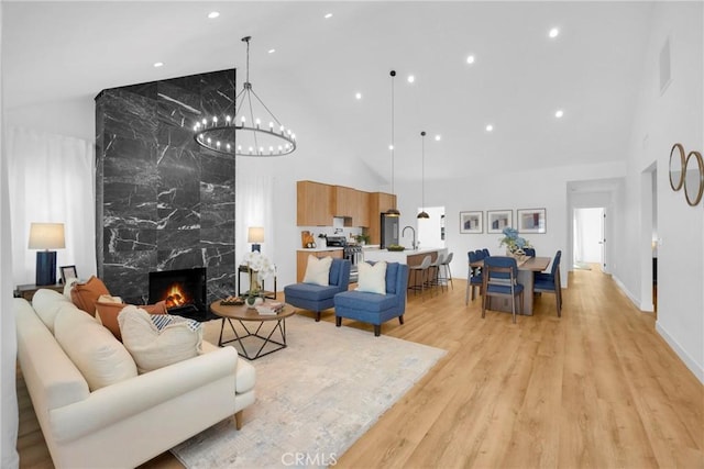living area with a high end fireplace, high vaulted ceiling, an inviting chandelier, and light wood finished floors