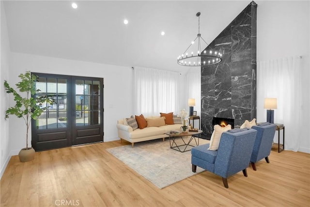 living room featuring a notable chandelier, a premium fireplace, high vaulted ceiling, baseboards, and wood finished floors
